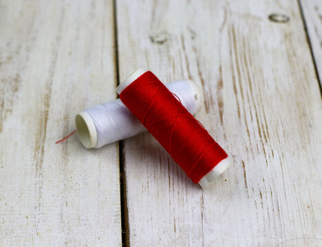 red and white sewing thread on a rustic wooden table.