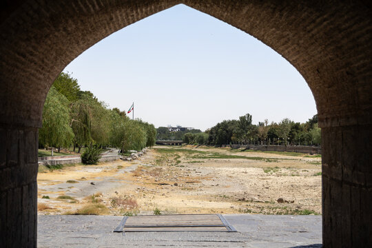 The Iranian flag waves near the dry bed of the Zayandeh River in Isfahan, iran, as drought and extreme summer heat have left the channel empty, illustrating water shortages and climate change impacts.