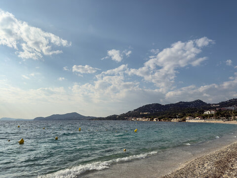 View across the Mediterranean Sea from Plage de l'Almanarre, in hyeres, france showing turquoise water, a sandy shoreline, coastal hills, houses and the Mont des Oiseaux area on the French Riviera.