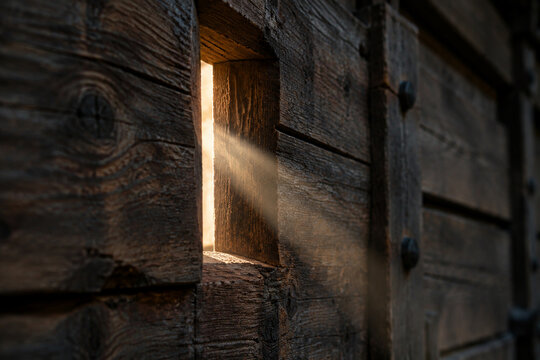 Close-up of a narrow arrow slit in a wooden wall, a single beam of light shining through, detailed wood.