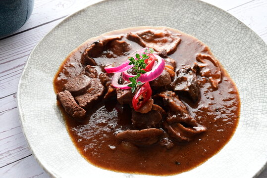 Traditional Czech cuisine featuring tender venison with mushrooms and bread dumplings served on a clean white plate.