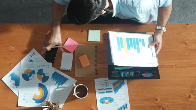 Top aerial view of manager working on laptop while looking at data analysis. Leader compare financial statistic graph while making decision at meeting table with document scatter around. Convocation.