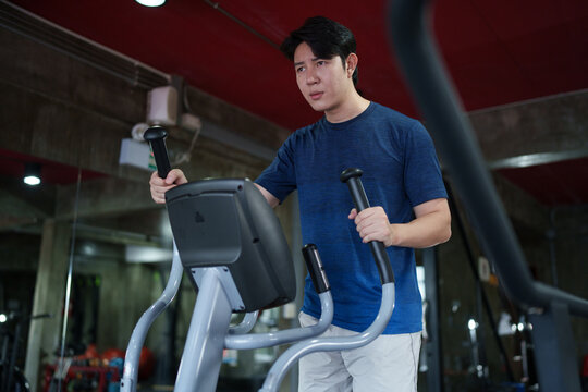 Young Asian man exercising on elliptical machine during cardio training session at fitness club
