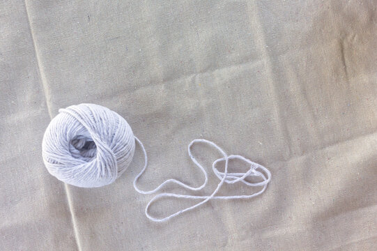 Ball of white yarn and loose thread on beige cotton fabric
