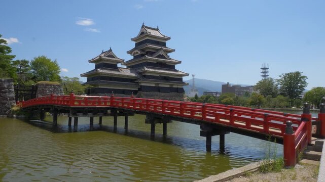 Matsumoto castle in japan with red bridge over moat under clear blue sky, historic landmark and popular tourist attraction.