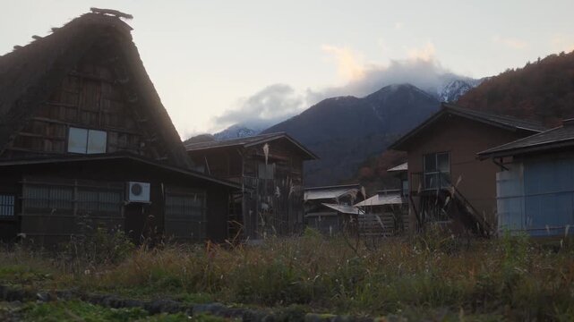 Traditional japanese village with old historic houses and a mountain range in the distance under a cloudy sky.