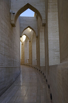A narrow, curving passage defined by pointed arches and textured limestone walls frames a pathway at the Museum of Islamic Art in Doha, Qatar