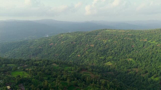 Aerial drone footage capturing the dense, forested slopes of the Western Ghats (Sahyadri mountain range) in India, blanketed in lush monsoon greenery with patches of exposed red laterite soil.