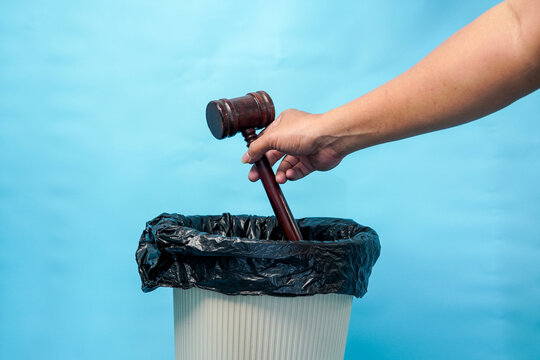 Hand throwing a wooden judge gavel into a trash bin representing legal system failure.