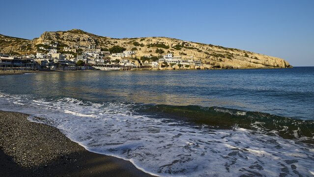 View of the sea and coastal village, impressive rock walls in the background, Matala, south coast, Crete, Greek Islands, Greece