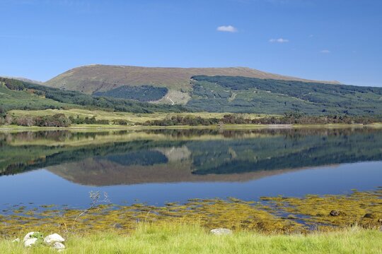 A loch with a clear reflection of mountains under a bright blue sky, Loch Eil, Scotland, Great Britain