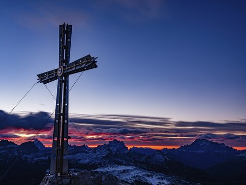 Sassongher summit cross at dawn, in the background Monte Cristallo, Monte Pelmo and Civatta, Dolomites, Trentino, South Tyrol, Italy