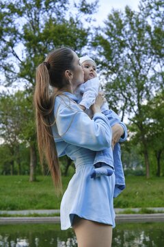 Mother lifts baby in arms while standing by water in park in evening. They enjoy time together with trees surrounding them