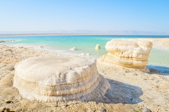 Dead Sea salt crystal formations on shoreline beach in Jordan on sunny mid-day with turquoise water desert coast. Lowest point on Earth landscape. Jordan - Israel border line zone
