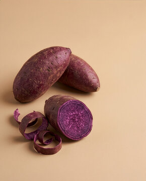 Purple Sweet Potato Sliced Open Revealing Vivid Violet Flesh, Raw Ubi Ungu Root Vegetable on Beige Background