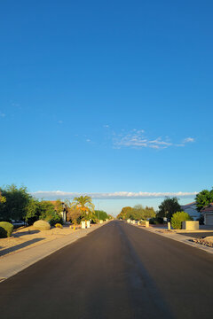 Long straight asphalt road stretches through a quiet desert suburban neighborhood under a bright blue sky with a thin line of clouds, Phoenix, AZ; copy space