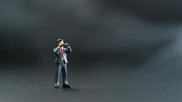 小さな双眼鏡を構えるミニチュアビジネスマン