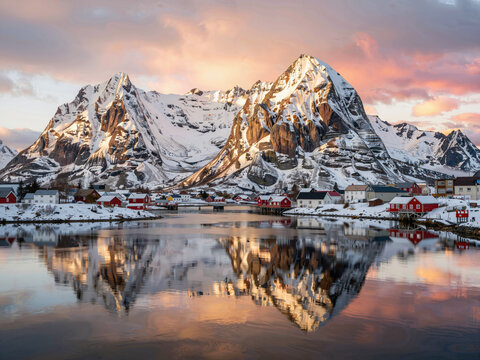 Reflection of red fishing village against snowy mountains at sunset