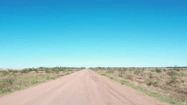 Unpaved dirt road stretching through expansive arid outback landscape under clear blue sky.