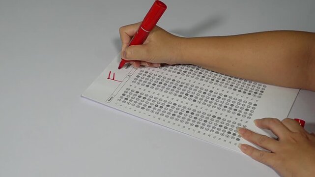 Close-up of teacher hand grading a multiple-choice exam with a red pen and giving an F failing grade.

