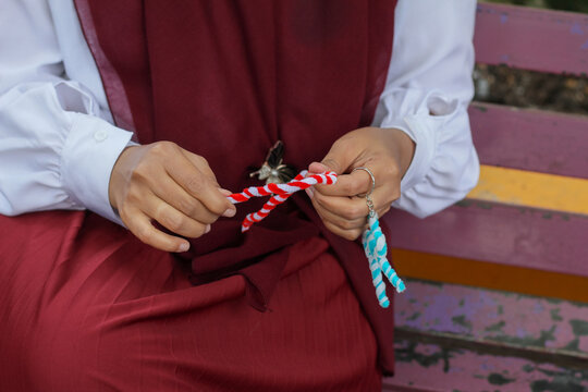 An Indonesian Muslim woman wearing a red hijab making pipe cleaner crafts on a park bench.