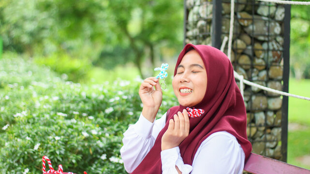 An Indonesian Muslim woman, a Muslim woman displaying a craft creation made from pipe cleaners, a Muslim woman wearing a red hijab.