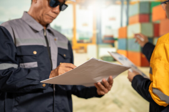 Construction workers in safety uniforms review paperwork outside a modern building, showing teamwork, inspection and project planning.
