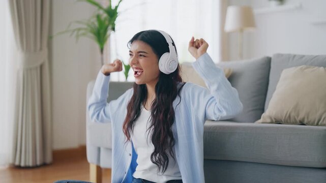Young asian woman listening to music on couch in living room at home. Happy asia female wearing headset and sitting on the floor