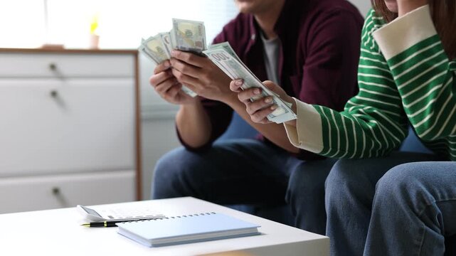 Young couple counting  banknotes while sitting on sofa at home.