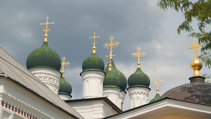 White church towers topped with green onion domes ornate golden crosses against moody gray clouds. Composition highlights architectural symmetry religious symbolism © VeNN