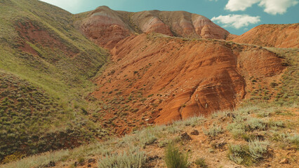 Vibrant red rock formations contrast with green shrubs under bright blue sky. Natural landscape with layered earth tones soft sunlight. Ideal for travel, nature, adventure themes © VeNN