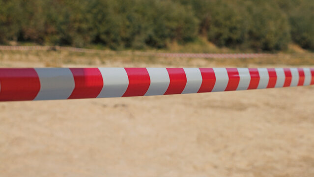 Red white striped barrier tape stretches across muddy racing track under natural daylight. Background shows blurred greenery. Shallow depth of field highlights tape