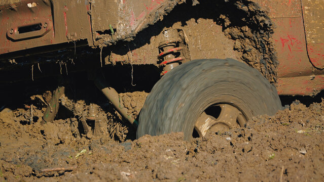 Close up of off road vehicle tire spinning rapidly in deep brown mud. Vehicle body covered in splattered mud under bright sunlight. Dynamic motion blur on tire conveys speed power