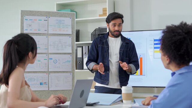 A diverse business team reviews an analysis presentation on a large screen, with a woman explaining data charts and growth plans to seated colleagues in a modern, organized office.	