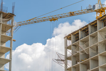 Building reaches for the sky as cranes work diligently against a backdrop of fluffy clouds © beholdereye