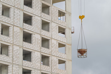 Construction workers elevate a concrete bucket at a building site in the heart of a bustling city under a cloudy sky © beholdereye
