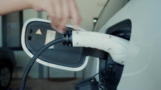 Person plugging in EV charging cable to white electric vehicle for sustainable energy transport.