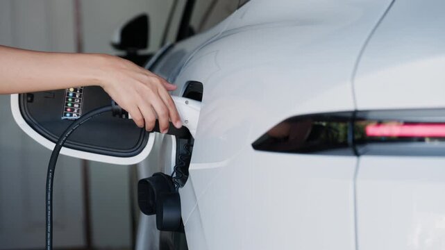 Person plugging in EV charging cable to white electric vehicle for sustainable energy transport.