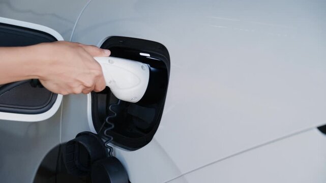 Person plugging in EV charging cable to white electric vehicle for sustainable energy transport.
