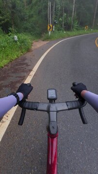 Cyclist riding on a winding road surrounded by lush greenery on a rainy day, showcasing outdoor adventure and nature.