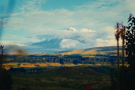 Cotopaxi volcano peak emerging from clouds over rolling hills in Ecuador