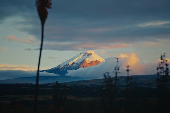 Cotopaxi volcano peak emerging from clouds over rolling hills in Ecuador