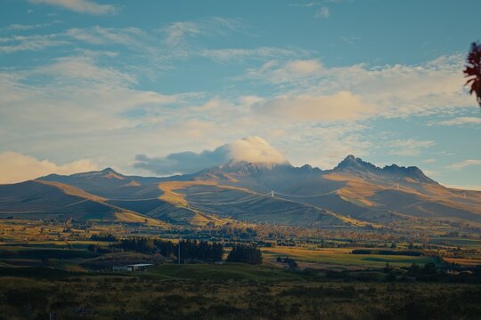 Cotopaxi volcano peak emerging from clouds over rolling hills in Ecuador