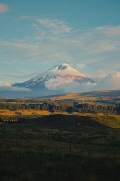 Cotopaxi volcano peak emerging from clouds over rolling hills in Ecuador