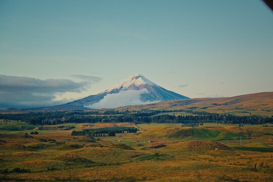 Cotopaxi volcano peak with snow and clouds over rolling hills in Ecuador