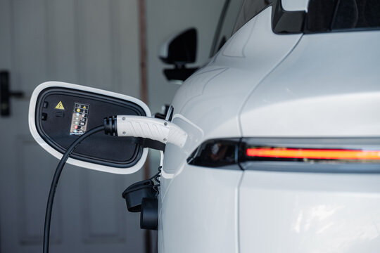 Person plugging in EV charging cable to white electric vehicle for sustainable energy transport.