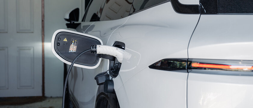 Person plugging in EV charging cable to white electric vehicle for sustainable energy transport.