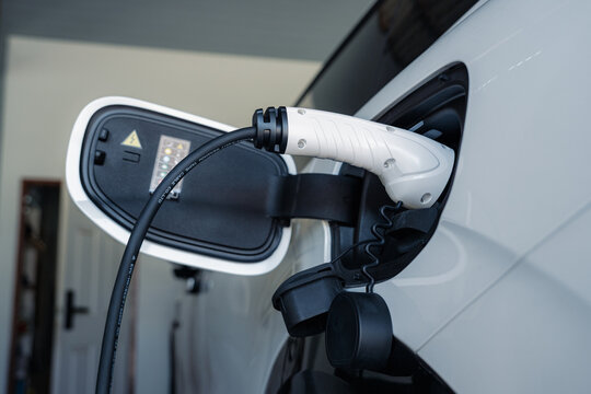 Person plugging in EV charging cable to white electric vehicle for sustainable energy transport.