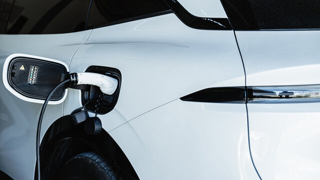 Person plugging in EV charging cable to white electric vehicle for sustainable energy transport.