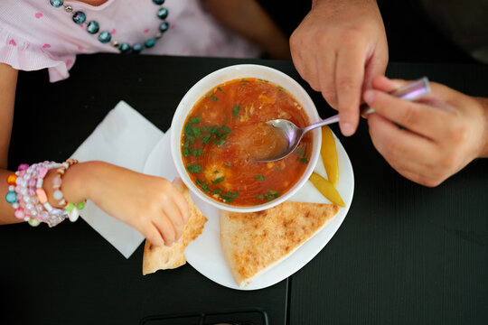 Family Sharing Traditional Soup Meal At Restaurant Table. Father and child eat red hot soup with bread inside a restaurant